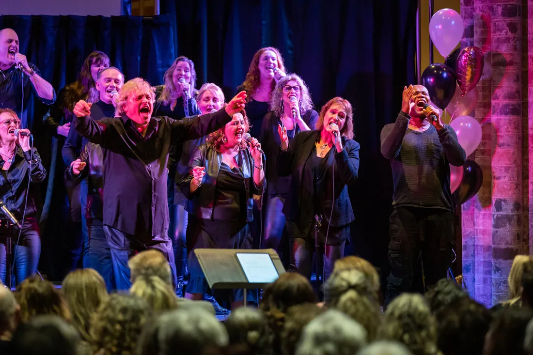 Zangers van Amstel Gospel Choir met hun armen omhoog tijdens een energiek kerstconcert